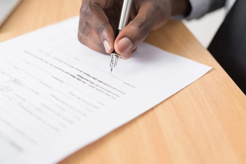 Firma de un contrato en papel que representa la formalización y los costes de compra de un inmueble en Portugal.